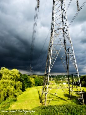 Electricity pylon with very dark sky and green grass