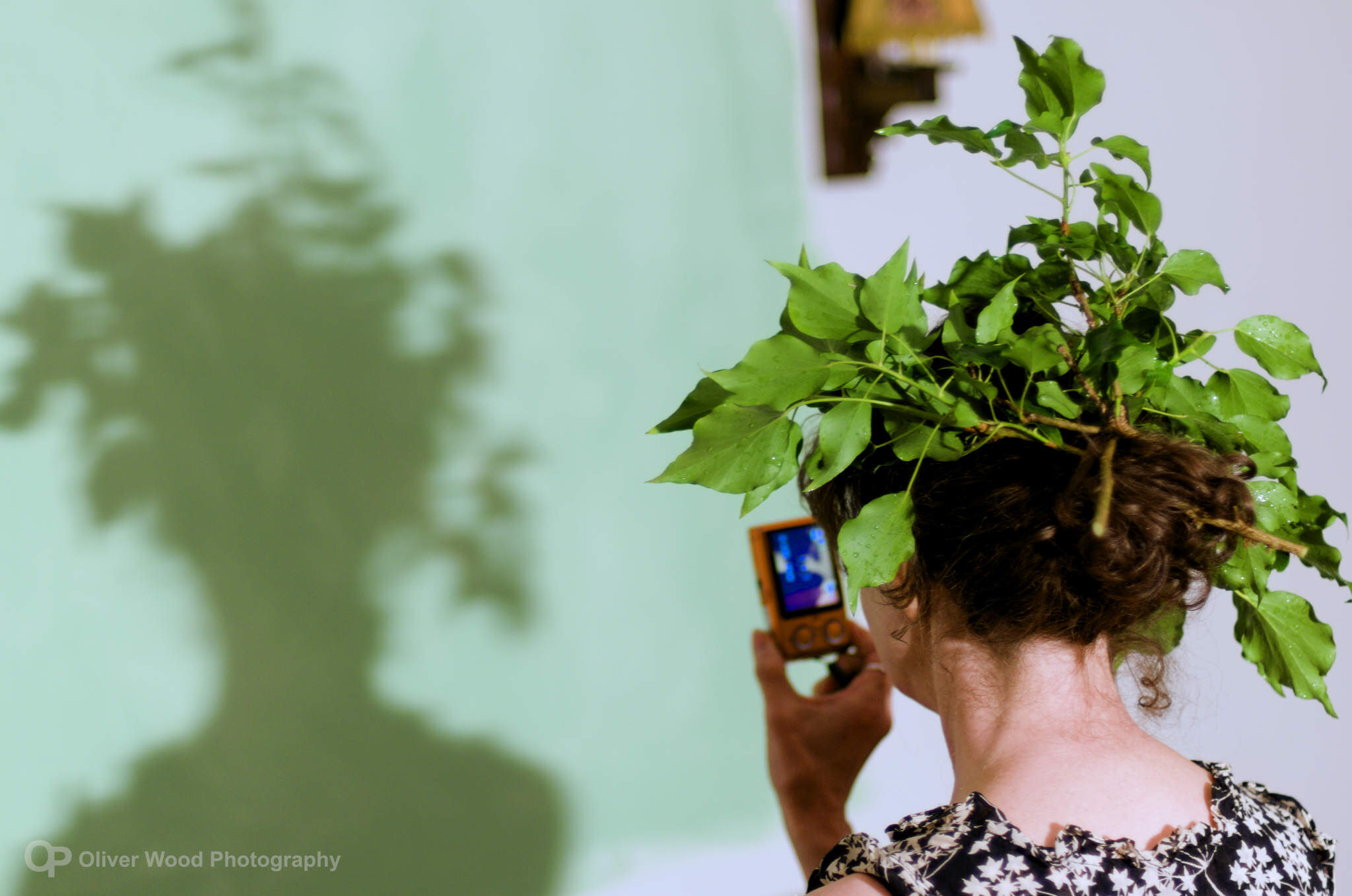 Woman with ivy in hair facing a green wall. 