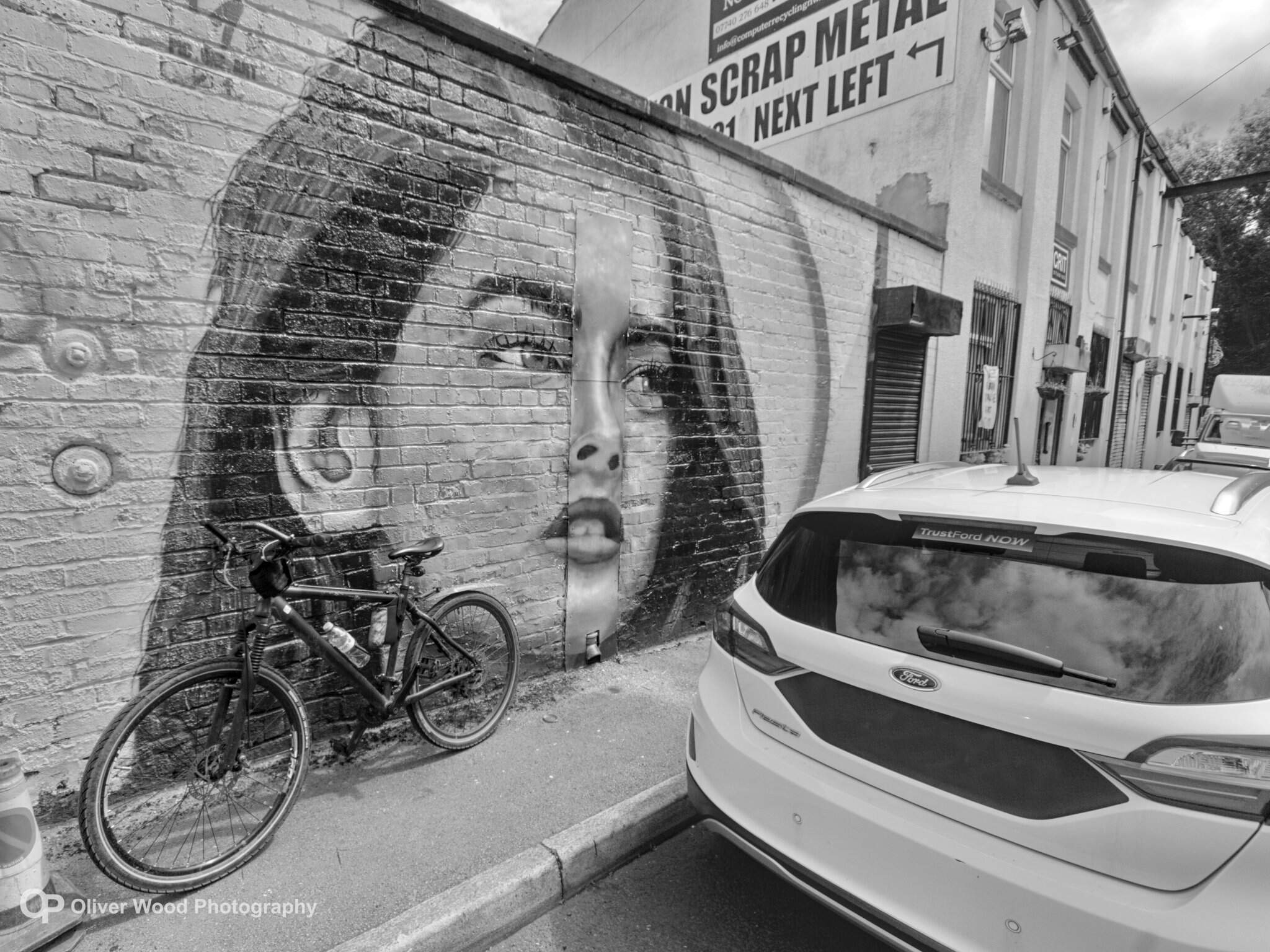 black and white image of a woman on a wall with bike and car
