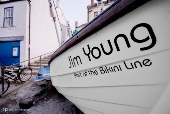 A fishing boat on dry land with buildings behind.
