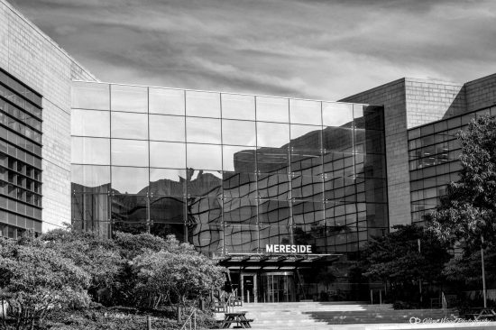 A black and white image of a glass sided building with reflections in glass